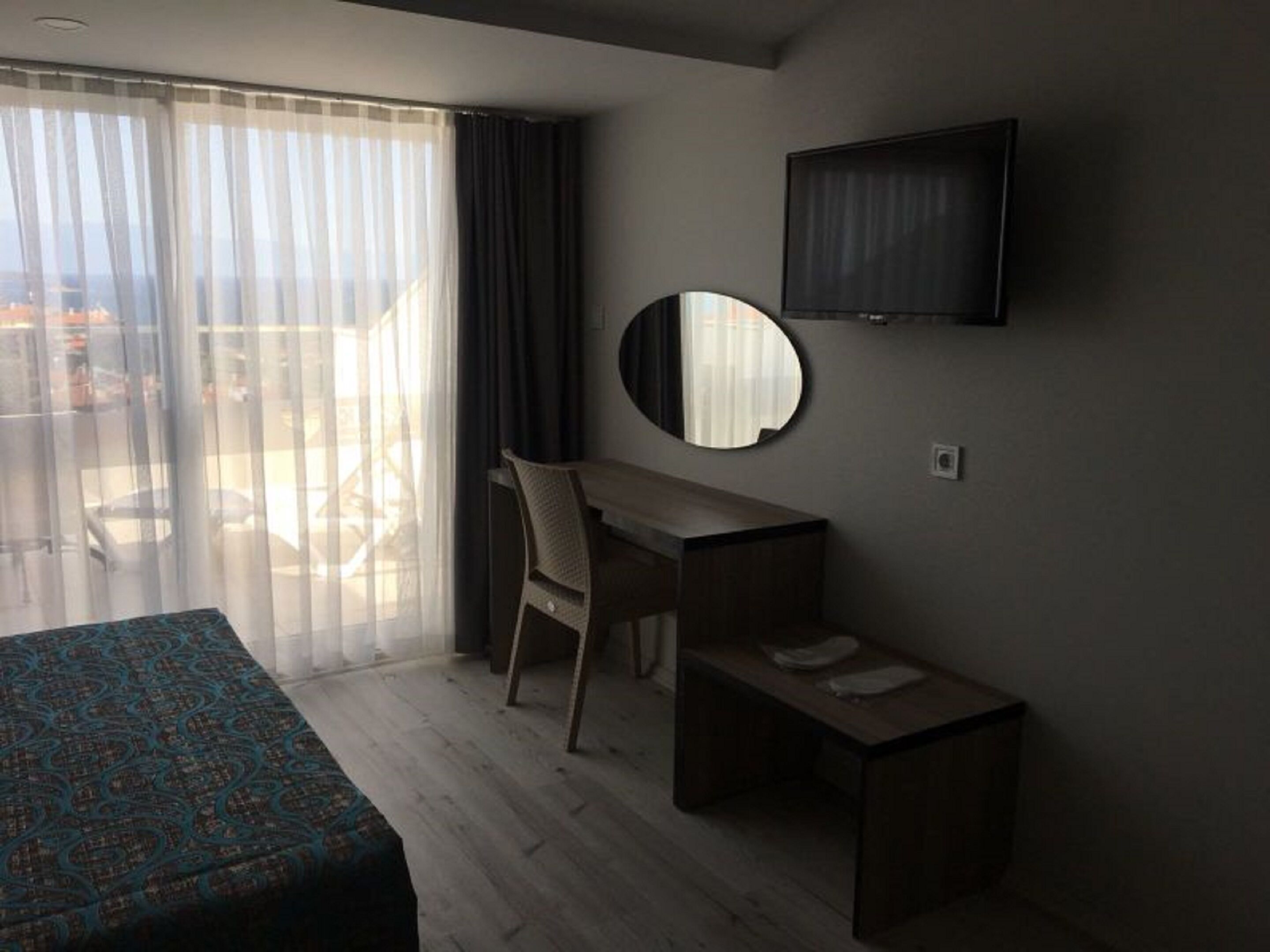 A hotel room with a bed, a desk, a chair, a TV, and a balcony with a view.