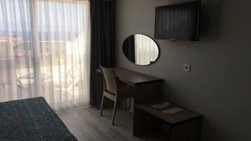Habitación de hotel con cama, escritorio, silla, televisión y balcón con vistas.