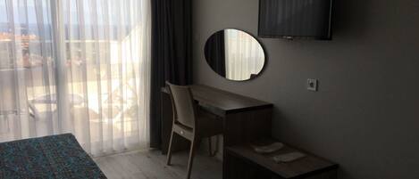 A hotel room with a bed, a desk, a chair, a TV, and a balcony with a view.