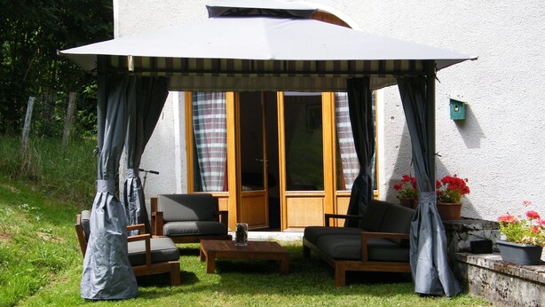 An outdoor seating area with a covered patio, two chairs, a table, and potted plants. - Maison Neuve Grandval - Gite (Grandval)
