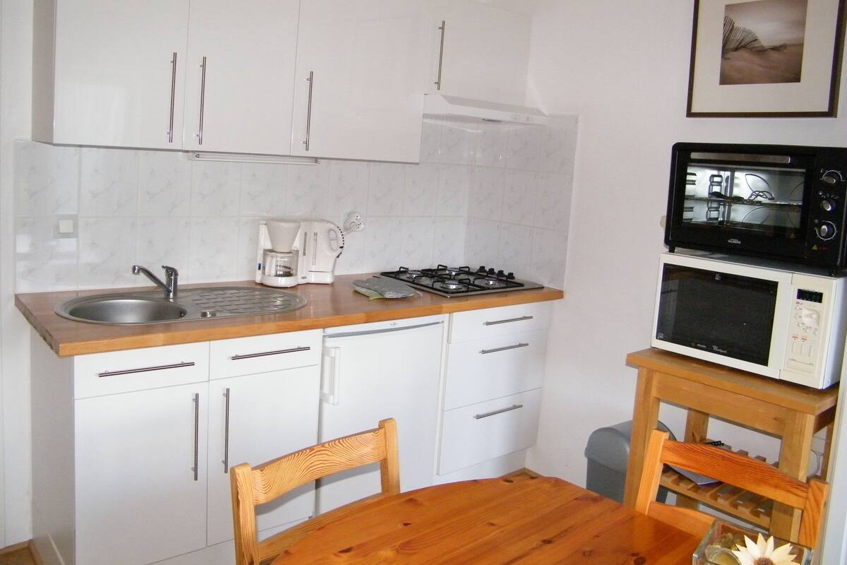 A compact kitchen with white cabinets, a wooden countertop, a sink, a coffee maker, a stove, and a microwave.