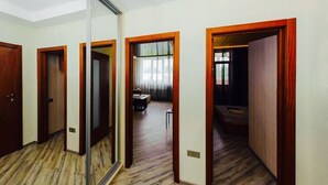 Un couloir d’hôtel avec un plancher en bois, des portes miroir et une vue sur une chambre où l’on aperçoit un lit et un bureau.