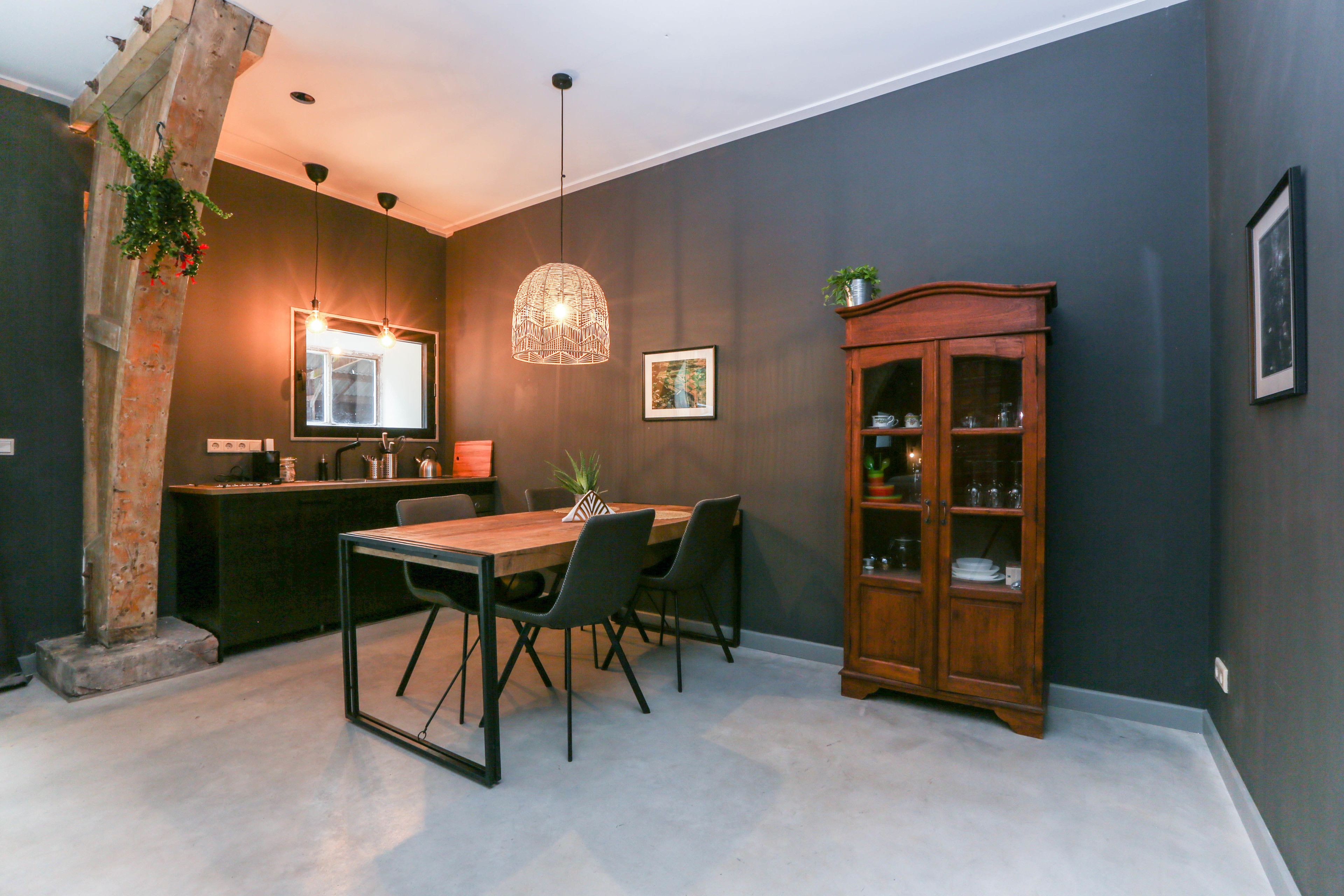 A dining area with a wooden table and chairs, a hanging light fixture, a wooden cabinet, and a brick pillar.