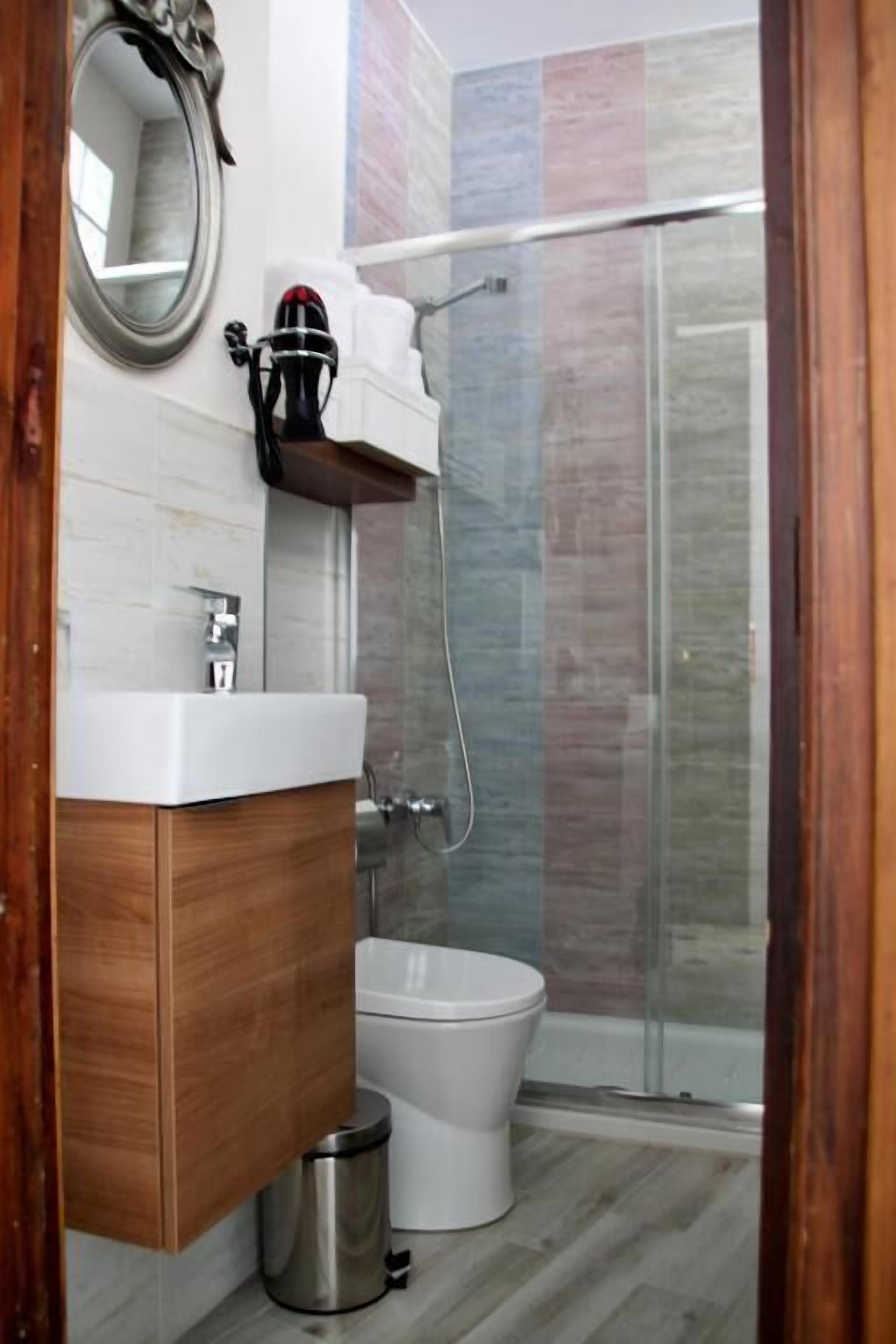 A modern bathroom with a wooden vanity, a white sink, a toilet, and a glass shower enclosure.