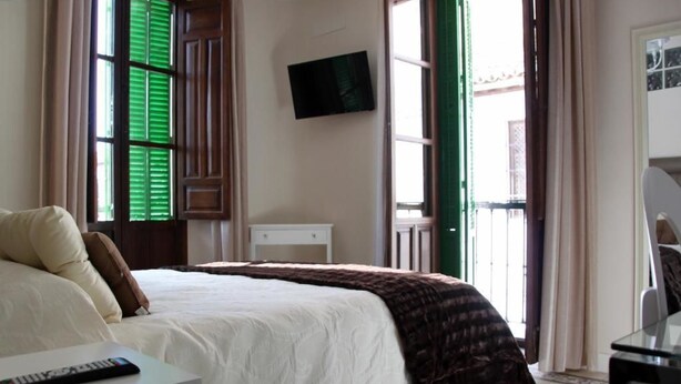 Une chambre d’hôtel avec un lit, un téléviseur fixé au mur, un bureau avec une télécommande et une fenêtre avec des volets verts.