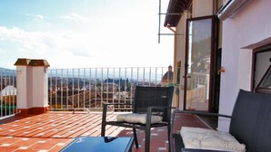 Un balcon avec une table et des chaises, une vue sur le paysage urbain et une porte donnant sur l’intérieur.