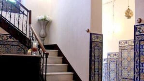 Un escalier recouvert d’un tapis rouge, un lustre et des murs ornés de motifs bleus.