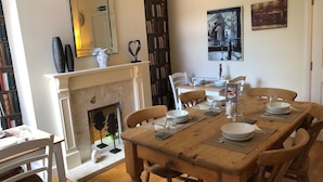 A dining room with a wooden table set for four, surrounded by chairs. A fireplace is visible in the background, and there are framed pictures on the wall. - 202 Guesthouse (Lincoln)