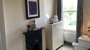 A bathroom with a white vanity, a black fireplace, a framed purple flower, and a window with curtains. - 202 Guesthouse (Lincoln)