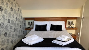 A neatly made bed with white linens, black pillows, and a black throw blanket. There are two bedside tables with lamps and a small clock. The room has patterned wallpaper and a wooden headboard. - 202 Guesthouse (Lincoln)