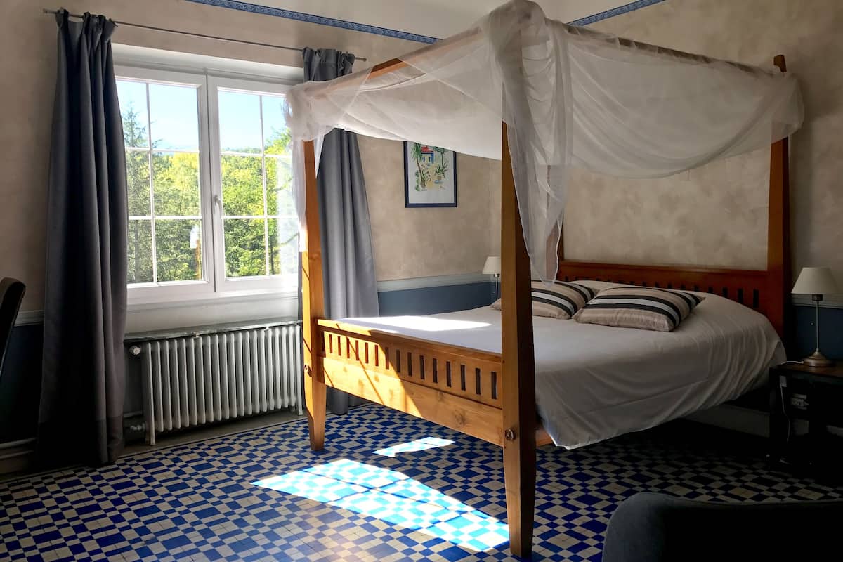 A four-poster bed with a canopy, a radiator, a checkered floor, and a window with curtains.
