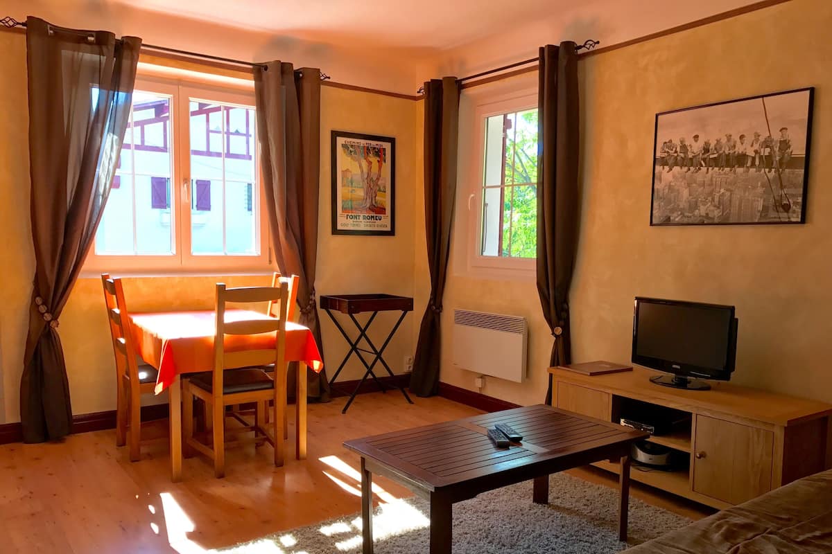 A cozy living room with a wooden table, a sofa, a TV, and a radiator.