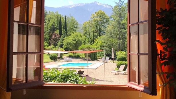 An open window with a view of a swimming pool, lounge chairs, and a mountainous landscape. - Villa du Parc (Prades)