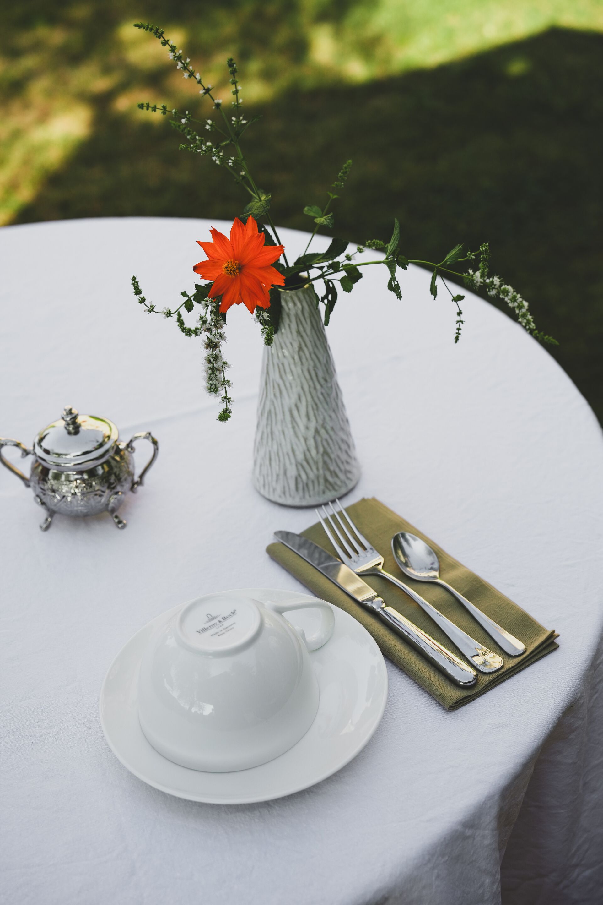 A table set with a white teapot, a white cup, and a gold napkin.