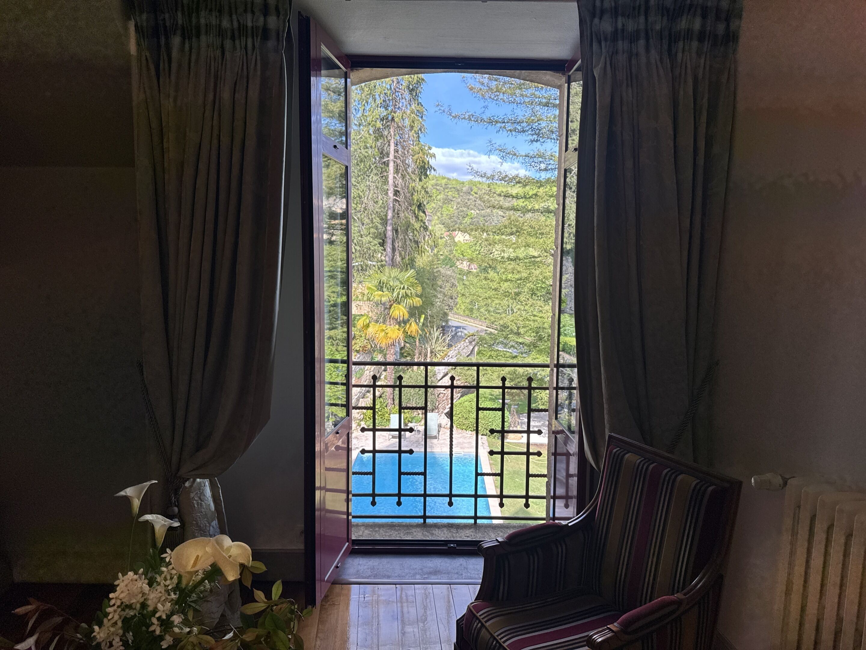 Una habitación con vistas a una piscina y follaje, una silla a rayas y un jarrón con flores.