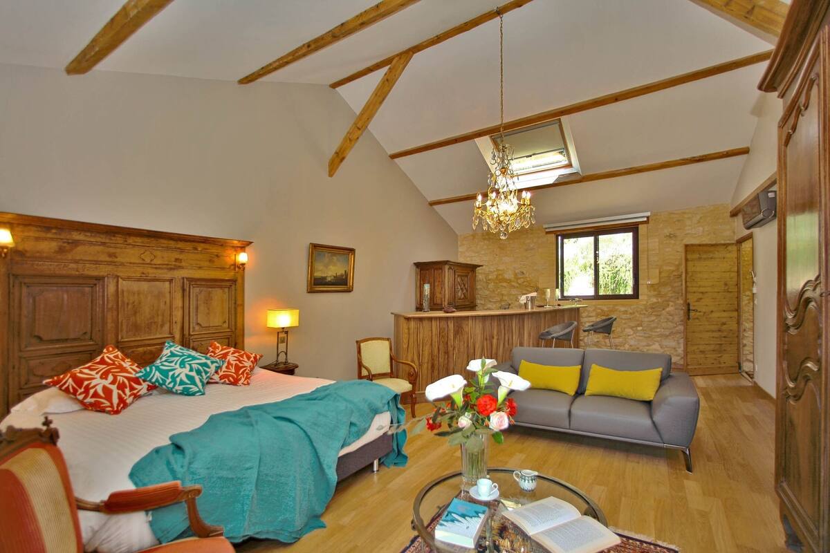 A cozy room with a bed, a sofa, a dining area, and a chandelier.