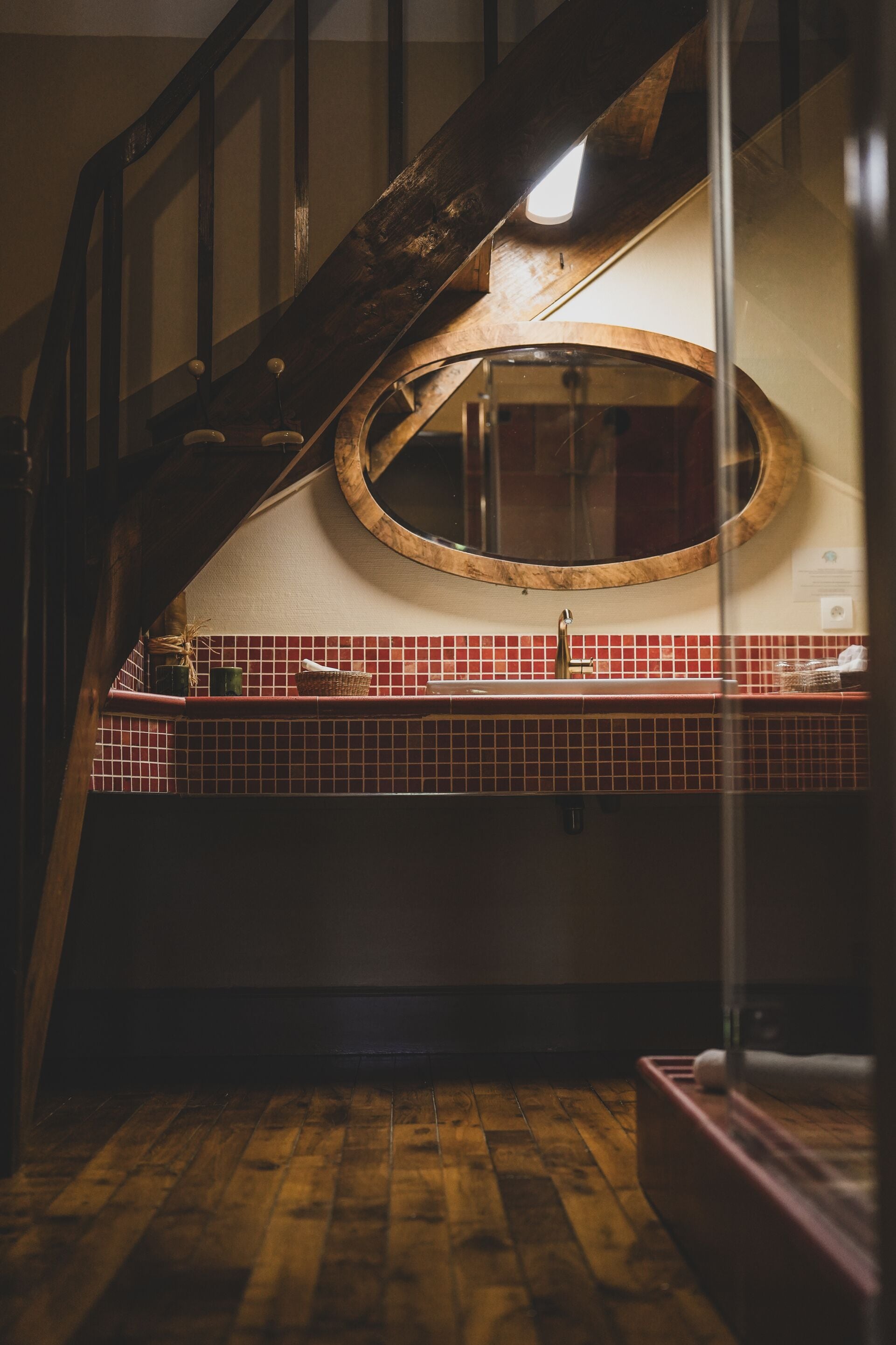 A wooden staircase with a circular mirror above a red-tiled sink.