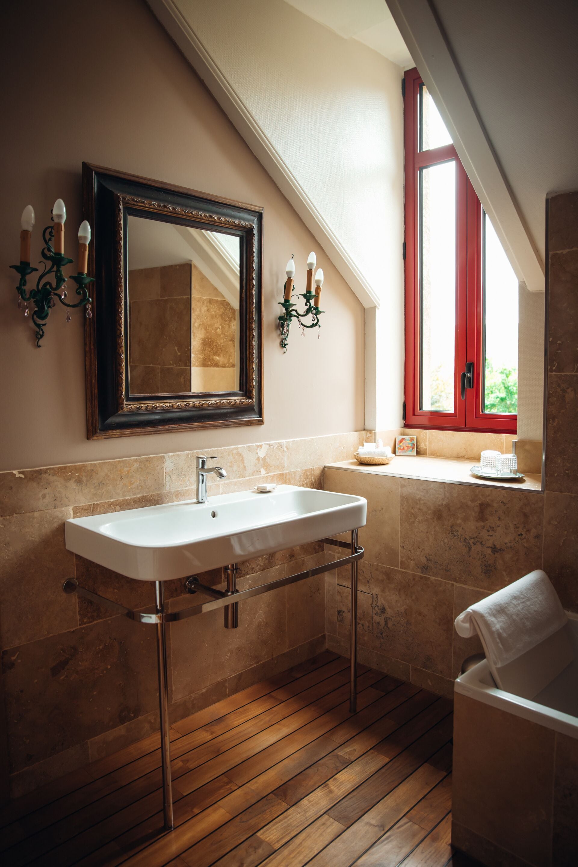 A bathroom with a white sink, a mirror, a window with red shutters, and a towel rack.