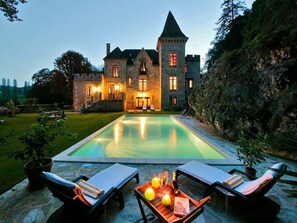 Un castillo de piedra con piscina y sillones de descanso.