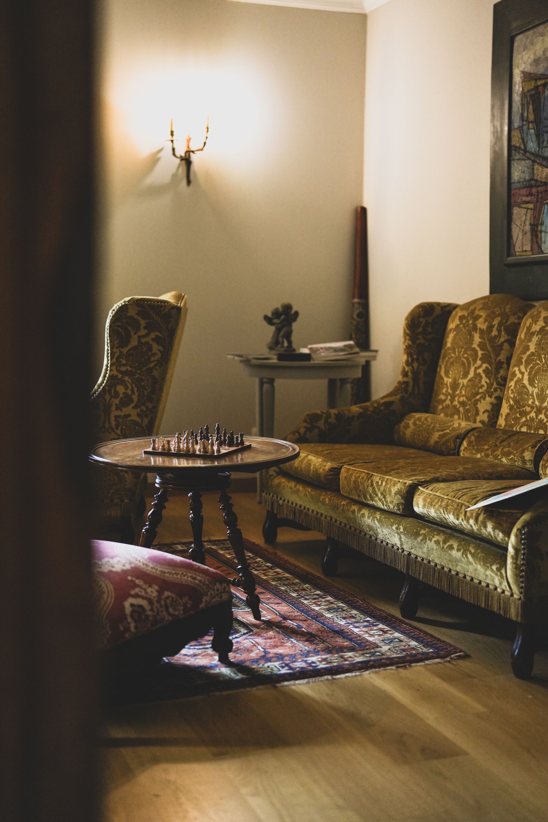 Une pièce avec un échiquier posé sur une table ronde, un fauteuil à motifs et un canapé recouvert d’un tissu à motifs.