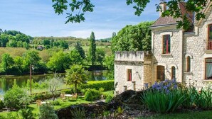 A stone building with a pond, surrounded by lush greenery and trees. - Manoir de la Malartrie (Vezac)