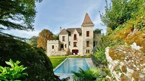 A castle-like building with a swimming pool, surrounded by lush greenery and a stone wall. - Manoir de la Malartrie (Vezac)