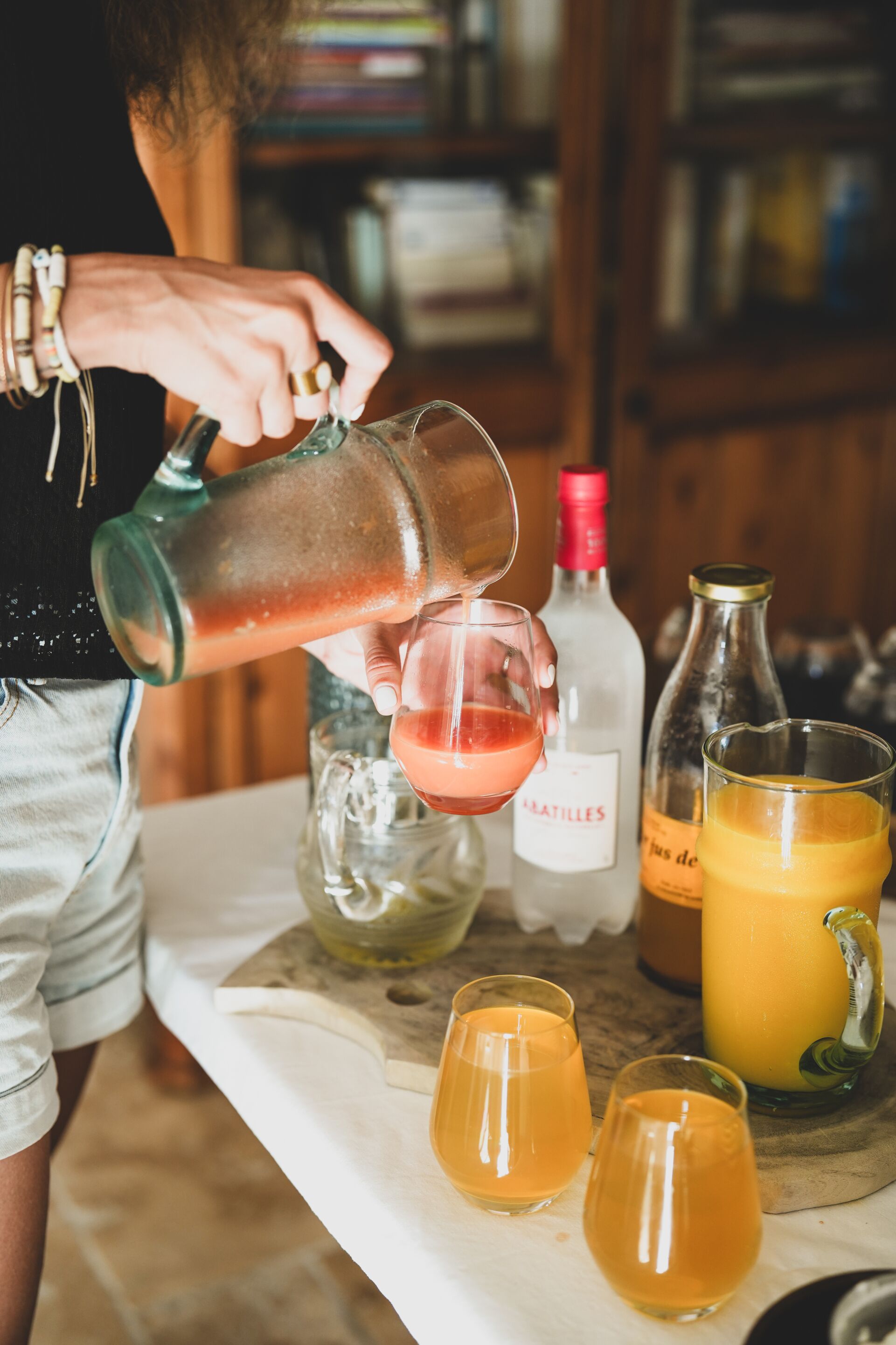 Une personne verse une boisson dans un verre, avec des bouteilles et des verres disposés sur une table.