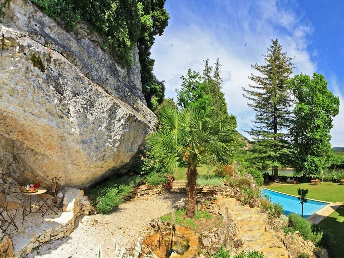Entorno natural al aire libre con piscina, una palmera y una gran formación rocosa.