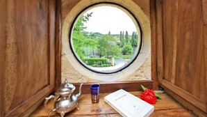 A wooden room with a round window, a teapot, a glass, and a book on the windowsill. - Manoir de la Malartrie (Vezac)