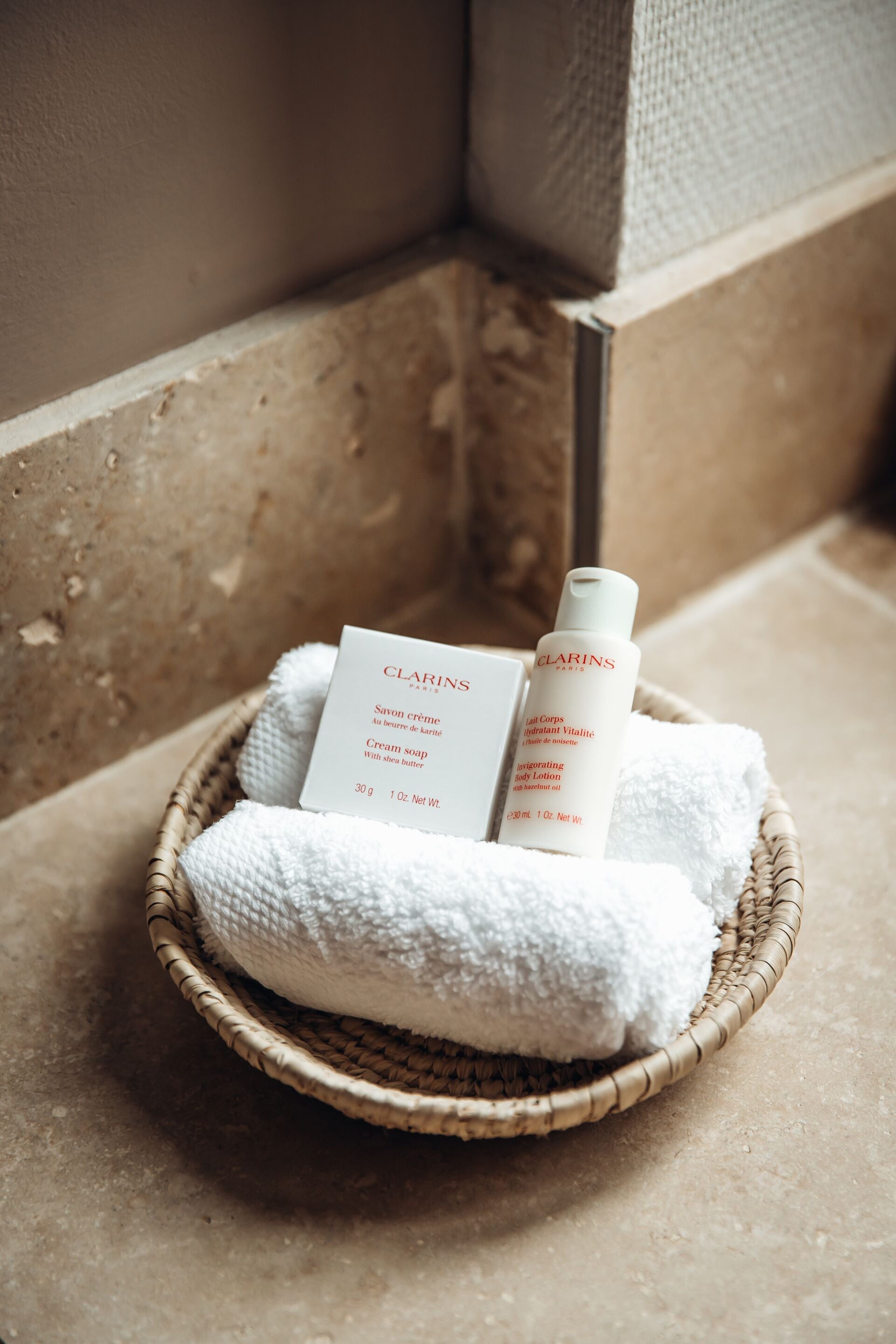 A wicker basket containing toiletries and a white towel, placed on a textured floor.