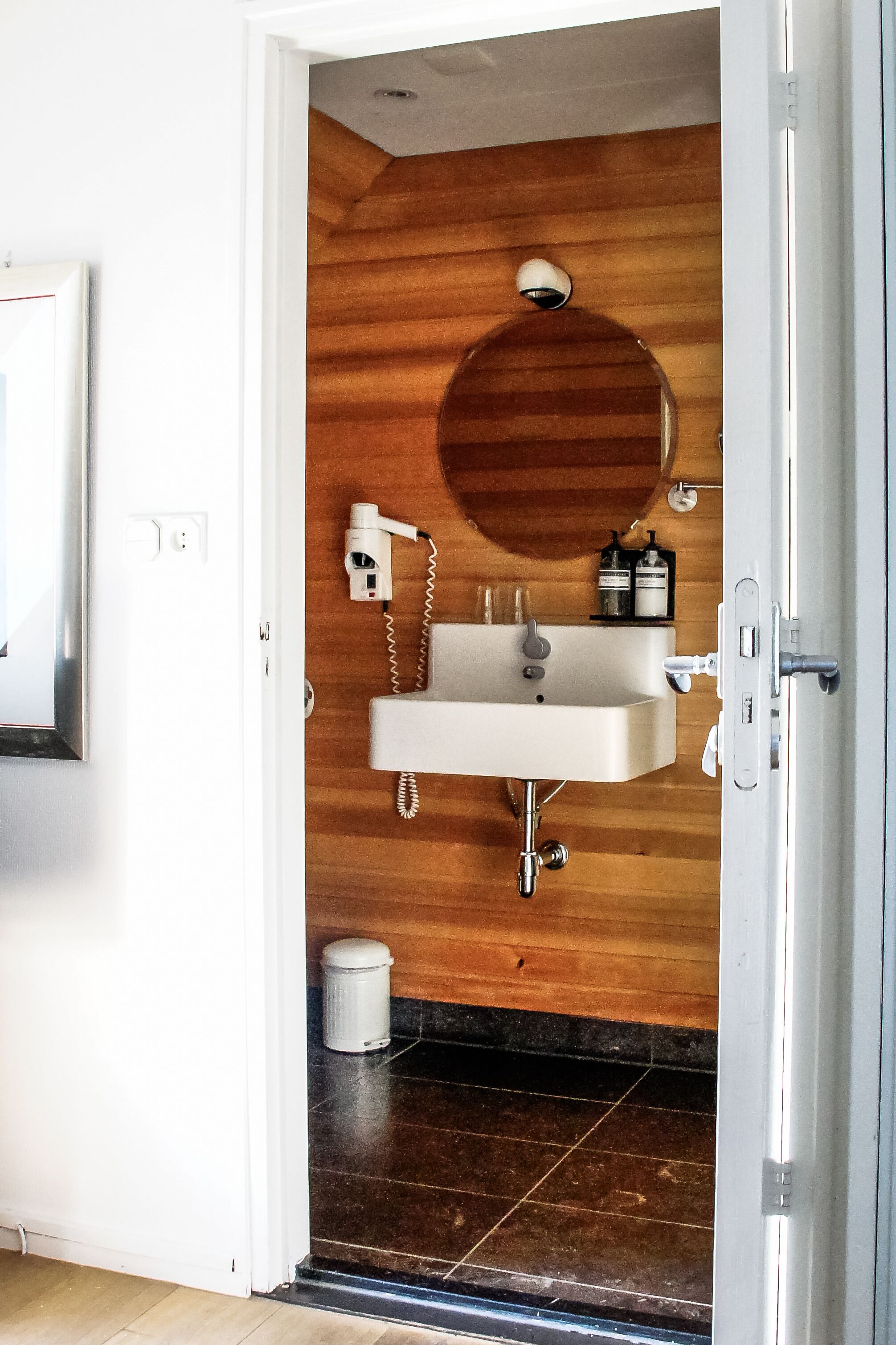 Ein Badezimmer mit einem Holzkosmetikschrank, einem Waschbecken, einem Spiegel und einem Föhn.