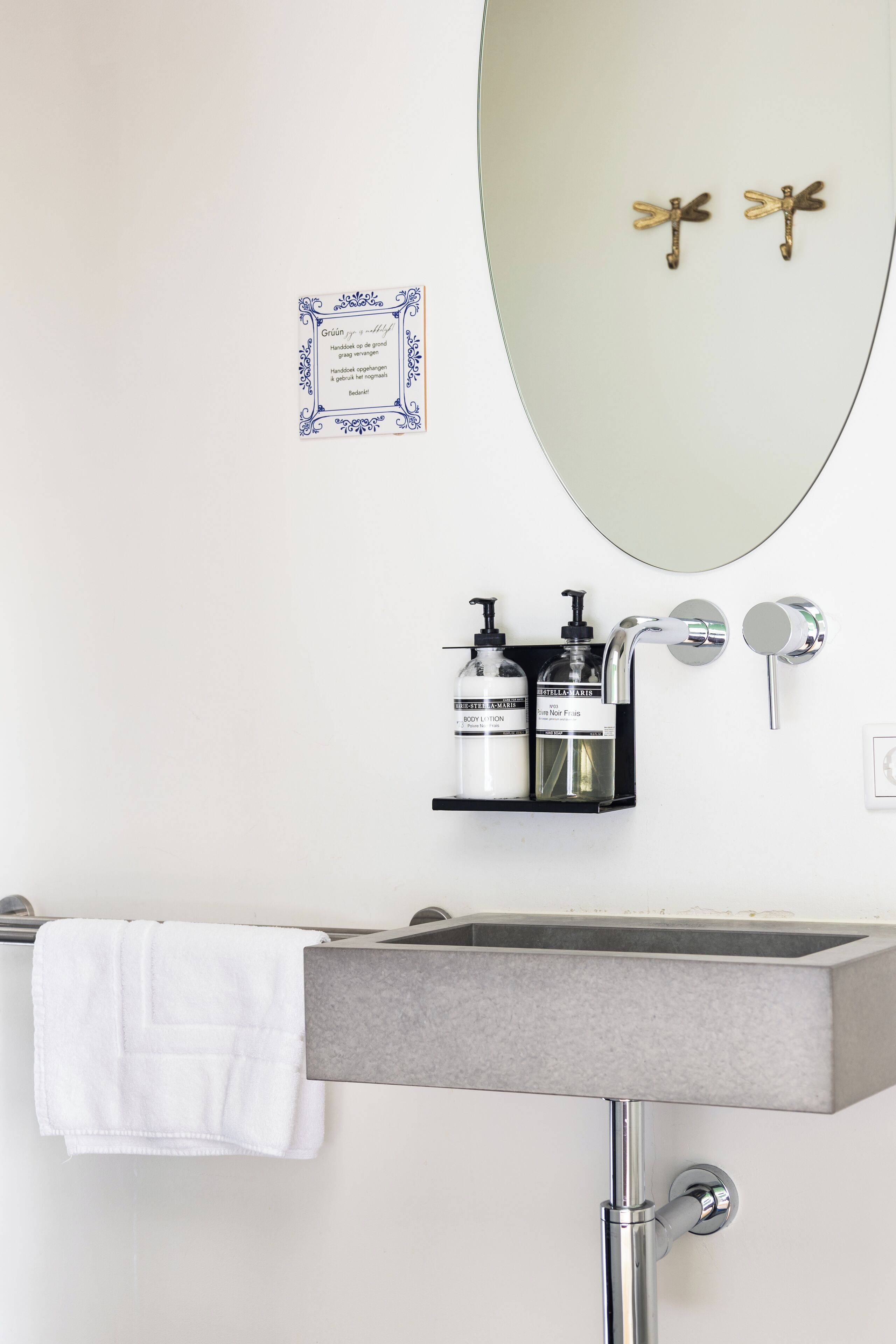 Une salle de bain avec un lavabo rectangulaire, un miroir et deux décorations murales en forme de libellule dorée.