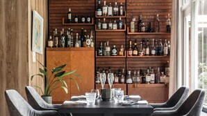 A modern dining area with a dark wooden table, grey upholstered chairs, and a wooden shelving unit displaying various bottles. - Hotel De Lochemse Berg (Barchem)