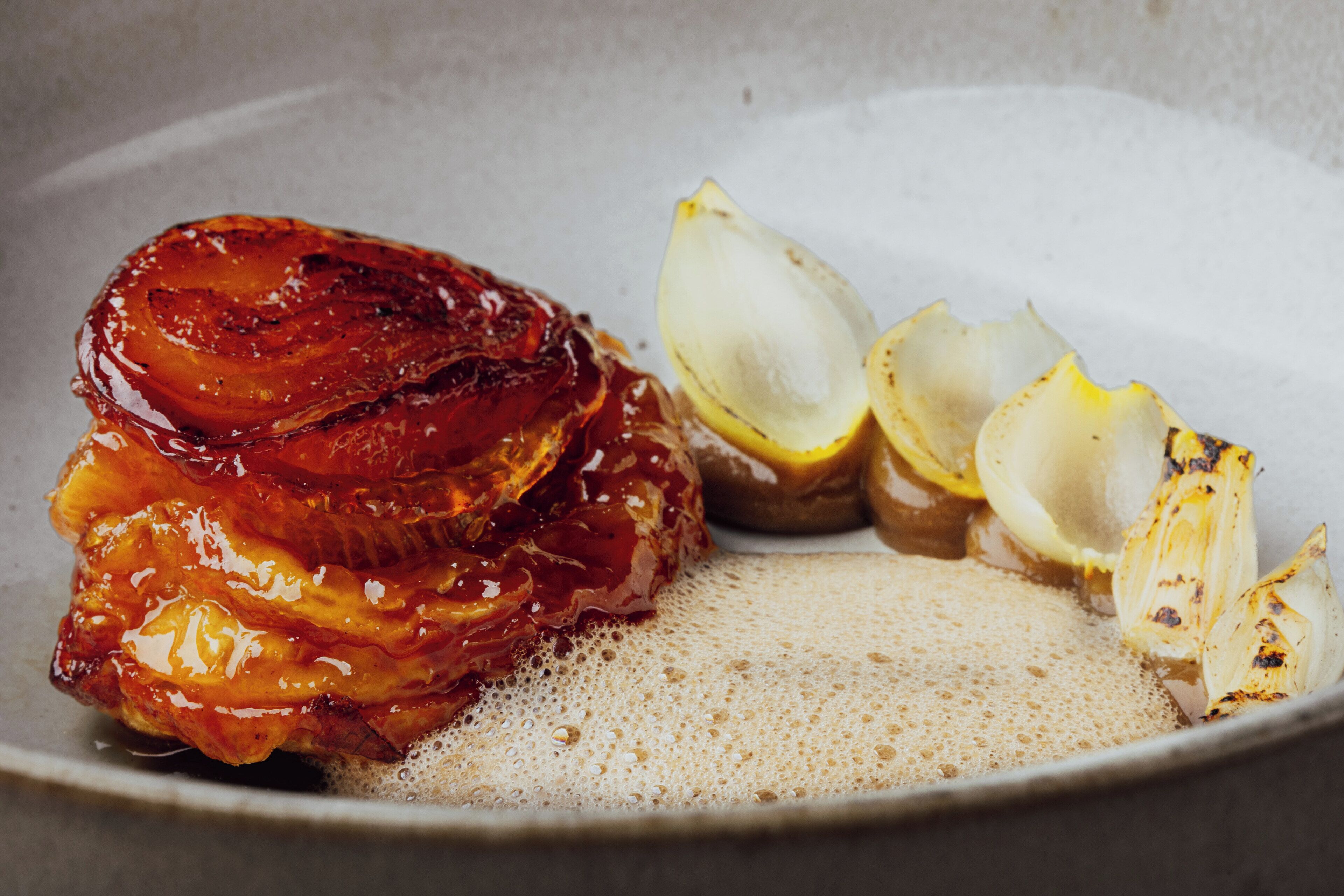 A plate with a glazed meat dish, lemon slices, and a creamy sauce.