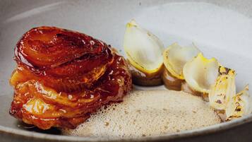 A plate with a glazed meat dish, lemon slices, and a creamy sauce.