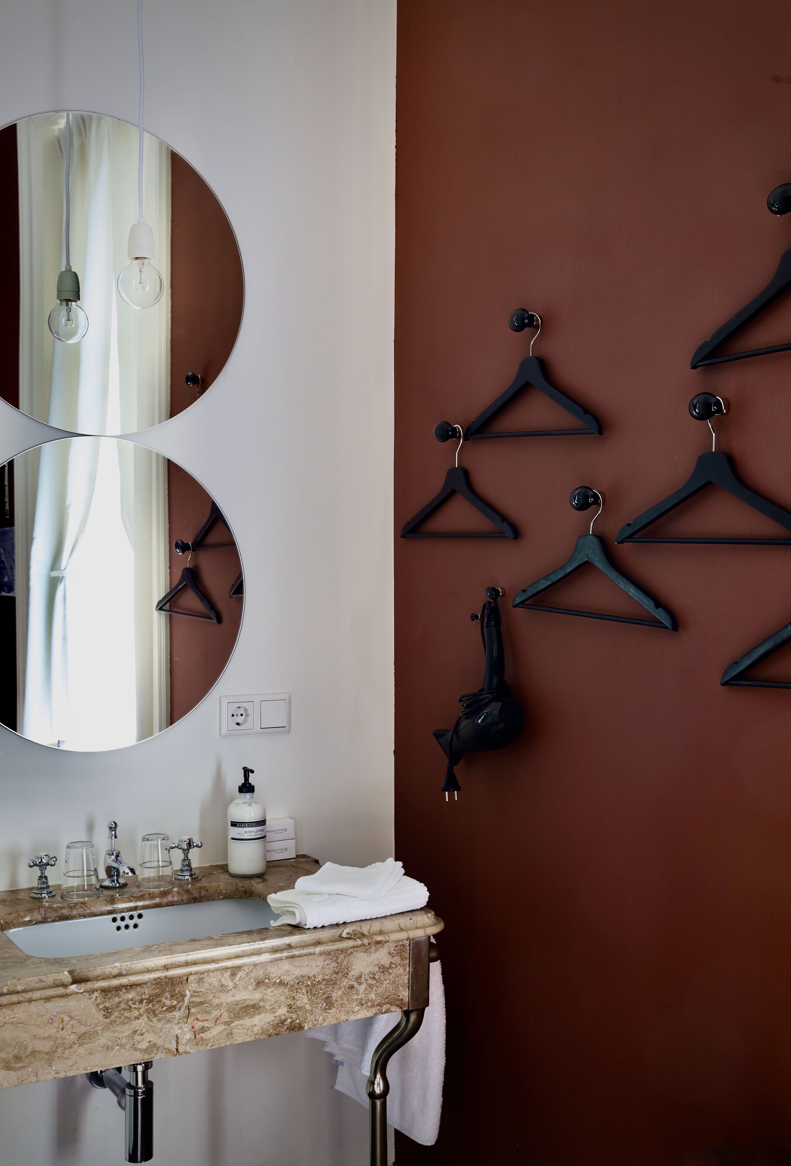 A bathroom with a sink, mirror, and multiple black hangers on the wall.