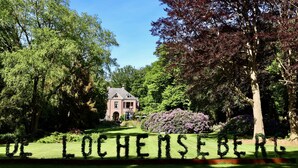 A building surrounded by lush greenery and a sign spelling "LOCHE MSE BERL." - Hotel De Lochemse Berg (Barchem)
