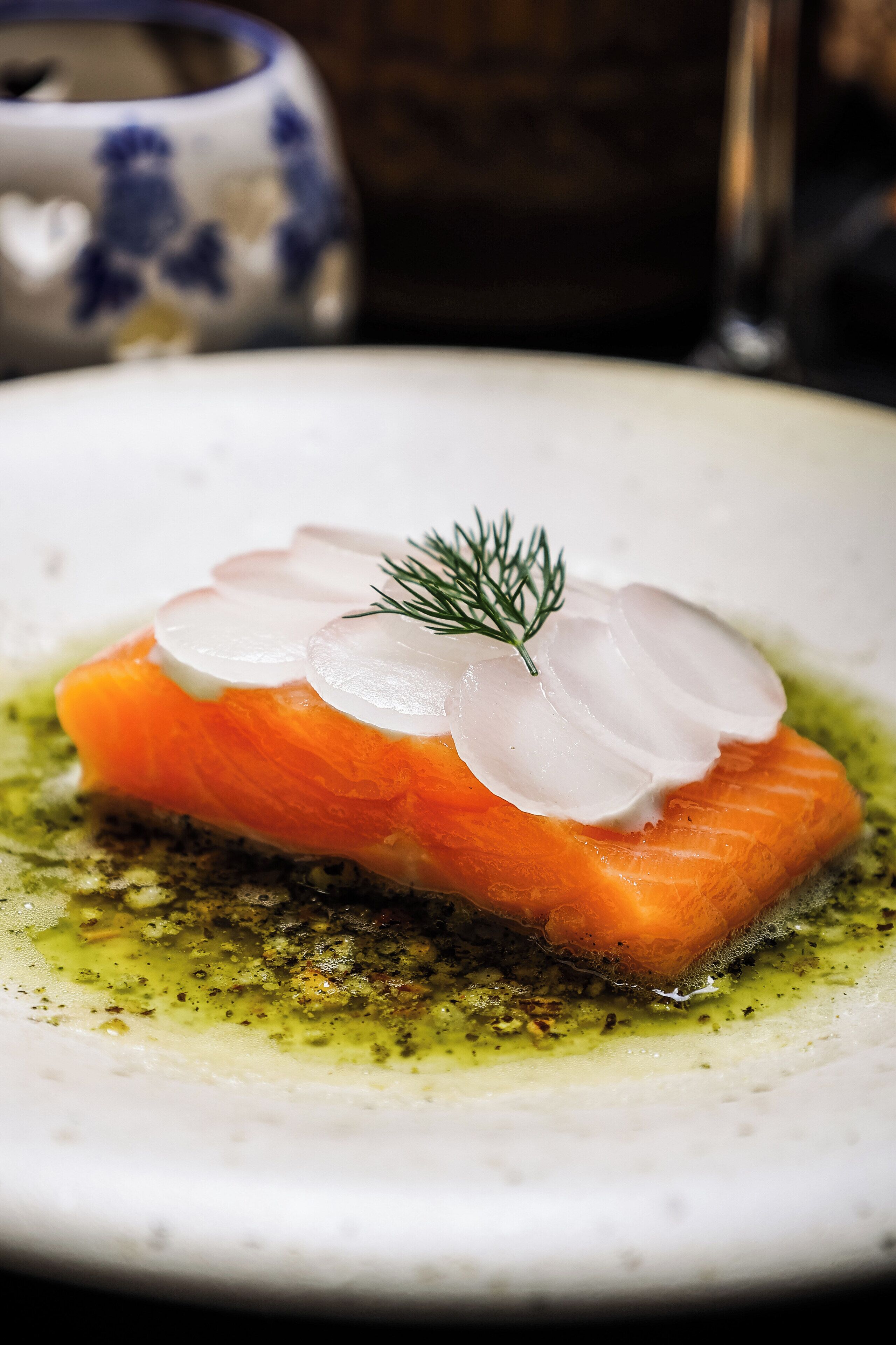 A plate of salmon with slices of white onion and a sprig of dill on a bed of green sauce.
