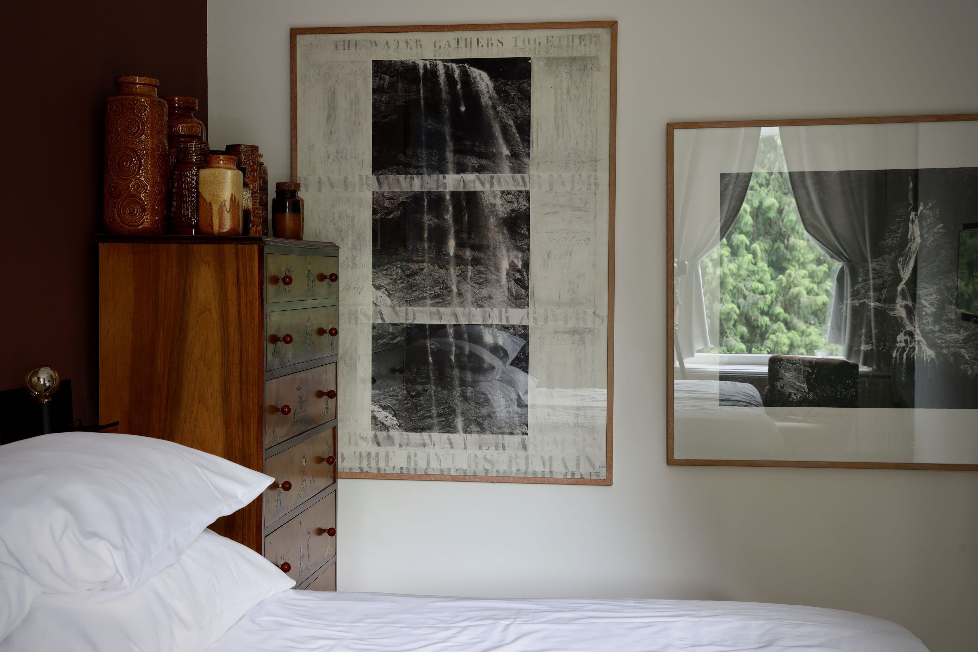 A bedroom with a bed, a dresser with drawers, a framed photograph on the wall, and a window with curtains.