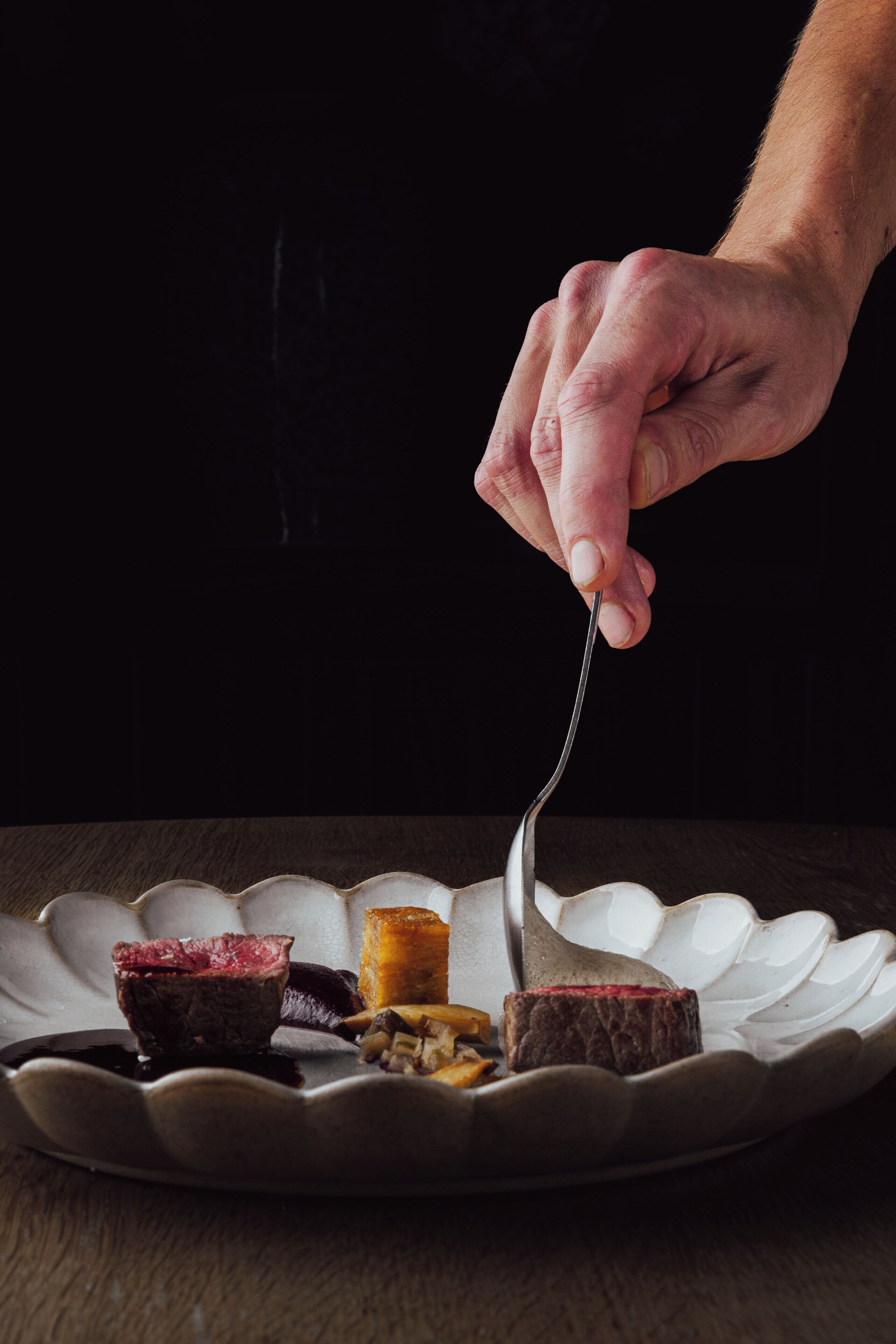 Une main tenant une fourchette au-dessus d’une assiette contenant différents aliments.