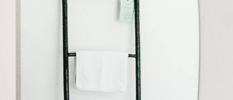 Un baño con un lavamanos moderno, una toalla colgada en un perchero y un espejo que refleja la zona del lavabo.