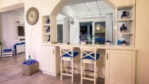 A kitchen with white cabinetry, two bar stools with blue cushions, and a decorative mirror above the counter. - White Passion Villa (Rhodes)