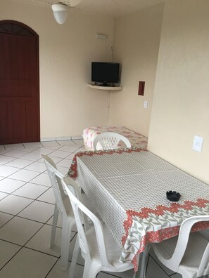 A small room with a single table and two chairs, a television mounted on the wall, and a door. - Pousada Dona Celia (Florianópolis)