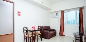 A small living room with a brown leather sofa, a wooden dining table with two chairs, a TV stand with a TV, and a window with curtains. - ZEN Home Beacon Makati (Makati)