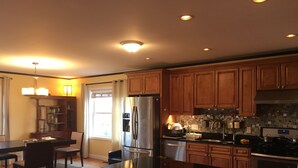 A modern kitchen with wooden cabinets, a stainless steel refrigerator, and a black countertop. - Rooms in Family House in Salem Boston (Saugus)