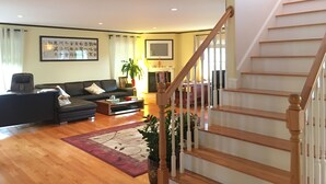 A spacious living room with a wooden staircase, a sofa set, and a large plant. - Rooms in Family House in Salem Boston (Saugus)