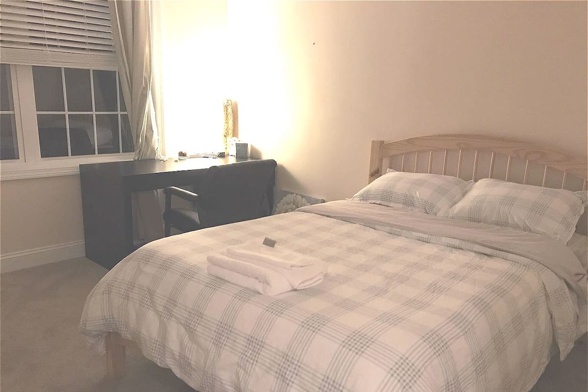 A bedroom with a bed, a desk, and a window.