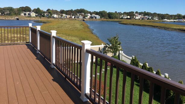 A wooden deck with white railings overlooking a calm lake, surrounded by grassy areas and houses. - Rooms in Family House in Salem Boston (Saugus)