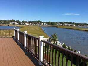 A wooden deck with white railings overlooking a calm lake, surrounded by grassy areas and houses. - Rooms in Family House in Salem Boston (Saugus)