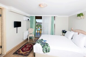 A hotel room with a large bed, a television mounted on the wall, a chair, and a view through a doorway. - Belizi Hotel (Urla)